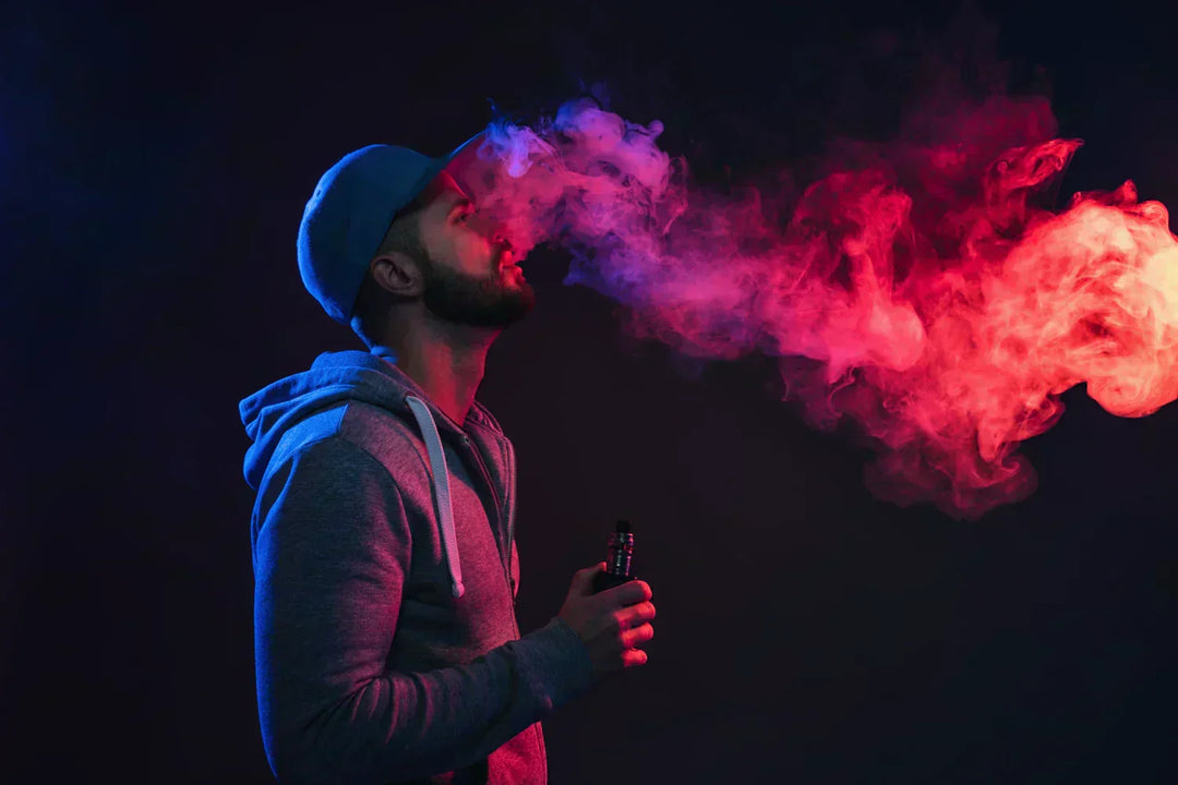  A colorfully-lit man smoking a vape with a trailing smoke floating in front of him